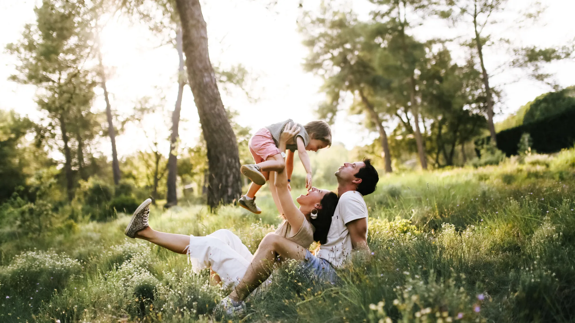 Parents jouant avec leur enfant dans l’herbe d’une pinède, séance famille en Provence