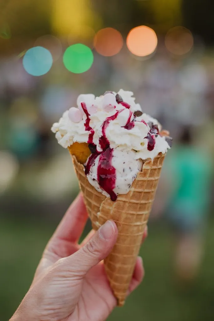 Cornet de glace artisanale tenu à la main, lumières de fête en arrière-plan