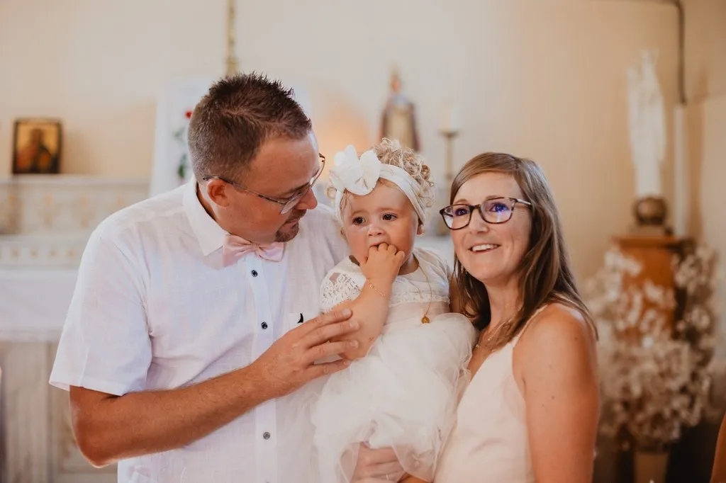 Parents et leur petite fille en robe blanche le jour du baptême