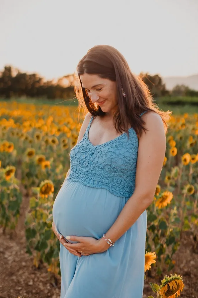 Future maman caressant son ventre dans un champ de tournesols au coucher du soleil