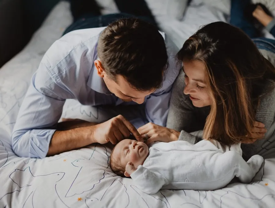 Jeunes parents penchés sur leur bébé allongé sur le lit, séance naissance à domicile