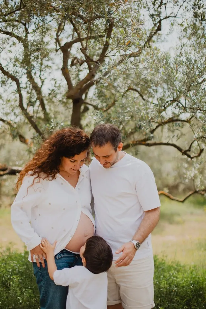 Futurs parents et leur aîné embrassant le ventre rond sous un olivier