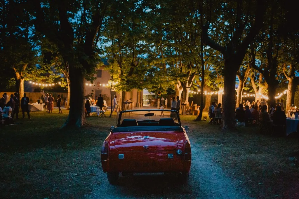 Voiture ancienne des mariés sous les arbres illuminés à la nuit tombée