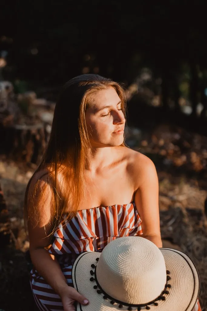 Portrait de jeune femme au soleil couchant, chapeau à la main
