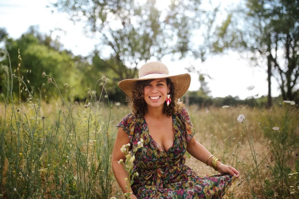 Femme souriante au chapeau assise dans les herbes hautes